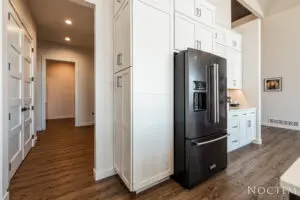 Black three doors fridge surrounded by white cupboards
