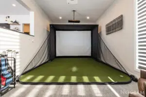 A room with a golf simulator and grass.