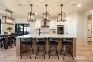A kitchen with five black stools and three lights.
