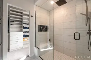 A walk in shower with glass doors and tiled walls.